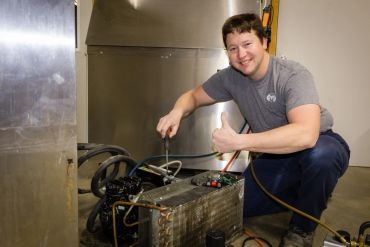 HVAC technician is smiling and giving thumbs up while happily repairing an AC unit.