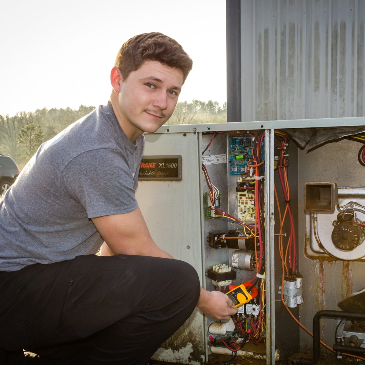 Burris Heat & Air worker smiling while using a multimeter.